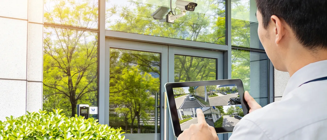 Technicien surveillant caméras de sécurité sur tablette près de fenêtres.