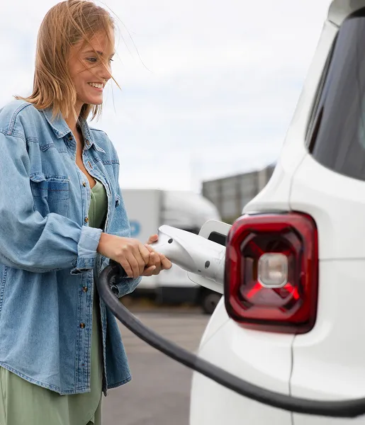 Femme souriant en train de recharger une voiture électrique.